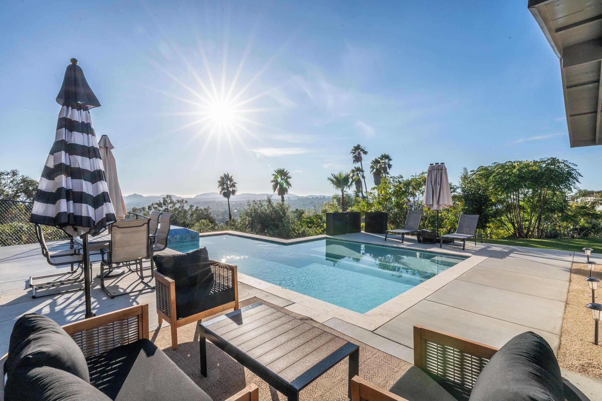 A swimming pool with lounge chairs and umbrellas, surrounded by palm trees and a clear sky.