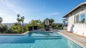 Una piscina con vistas a montañas, rodeada de palmeras y un patio con sillas de descanso.