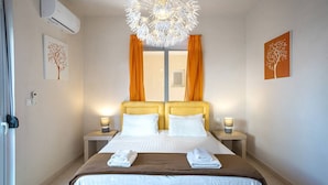 A hotel room with a double bed, two bedside tables with lamps, a modern chandelier, and artwork on the walls. - Kalives Sand - Beachfront apartment (Chania)