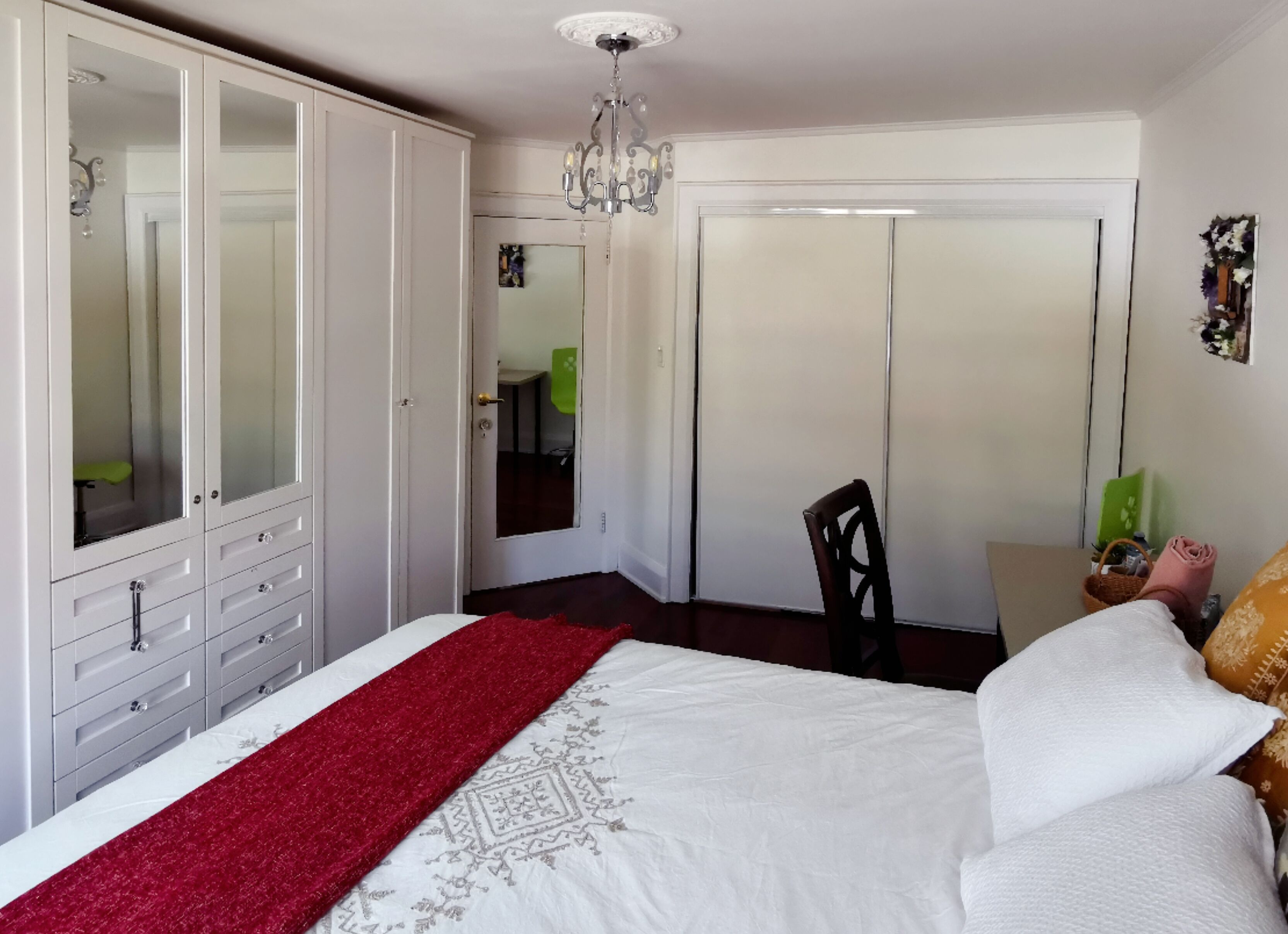 Een slaapkamer met een bed, een kledingkast, een spiegel, een kroonluchter en een deur.