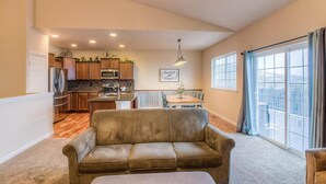 A living room with a brown sofa, a dining area with a table and chairs, a kitchen with wooden cabinets, and large windows with curtains. - Perfect 3-bedroom house with Gorgeous Views in Selah (Selah)