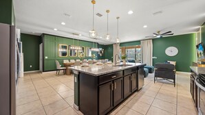 A modern kitchen with a central island, pendant lighting, and a dining area with chairs and a table. - Upstay Epic Windsor Home w Pool, Cinema & Games (Kissimmee)