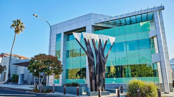 A modern building with a glass facade, a unique sculpture in front, and a clear blue sky.