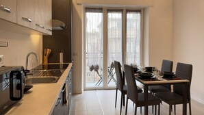 Una cocina moderna con horno integrado, un comedor con mesa dispuesta para cuatro personas y un puerta corrediza de vidrio que da a un balcón exterior.