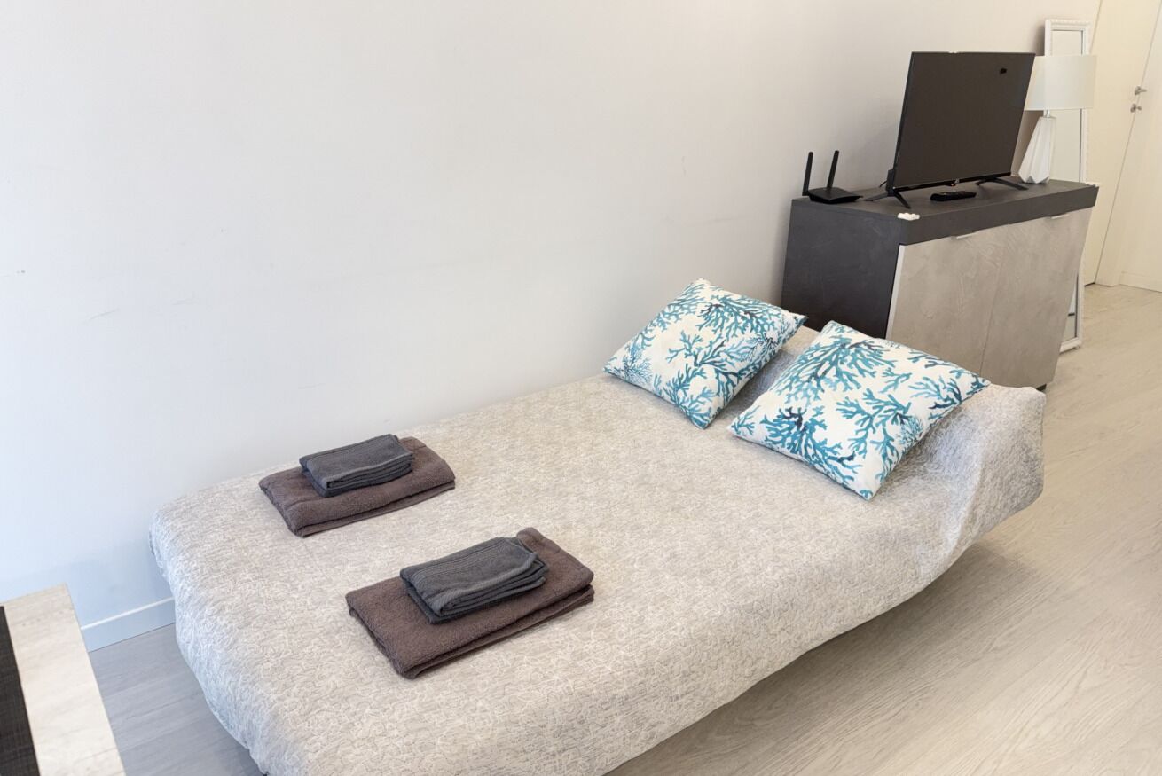 Un lit recouvert d’une couverture à motifs, deux oreillers à motifs de feuilles et deux serviettes pliées.