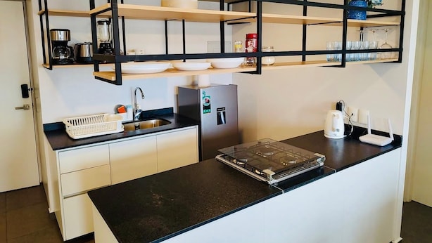 Eine moderne Küche mit schwarzen Arbeitsplatten, weißen Schränken und einem eingebauten Herd. Über der Arbeitsfläche befinden sich Regale mit Geschirr und einer Kaffeemaschine.