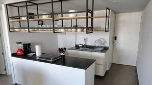 Una cucina moderna con isola centrale, piani neri, mobili bianchi e una scaffalatura in metallo nero sopra l'isola.
