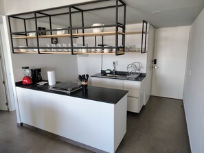 Eine moderne Küche mit einer zentralen Kochinsel, schwarzen Arbeitsplatten, weißen Schränken und einem schwarzen Metallregal darüber.