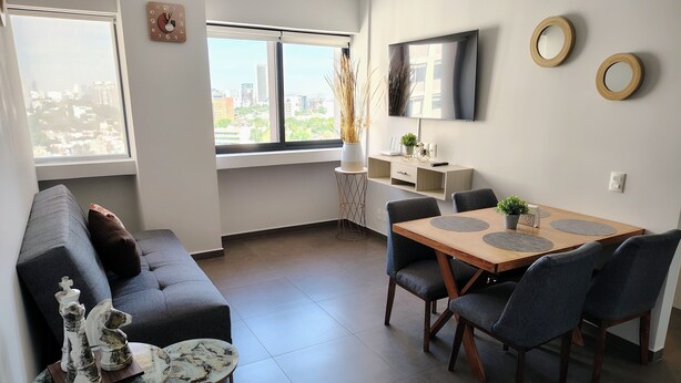 Un soggiorno moderno con divano, tavolo da pranzo con sedie, TV a parete e finestra con vista sulla città.