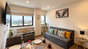 Ein modernes Wohnzimmer mit einem grauen Sofa, einem Esstisch gedeckt mit Tellern, Gläsern und einer Blumenvase.
