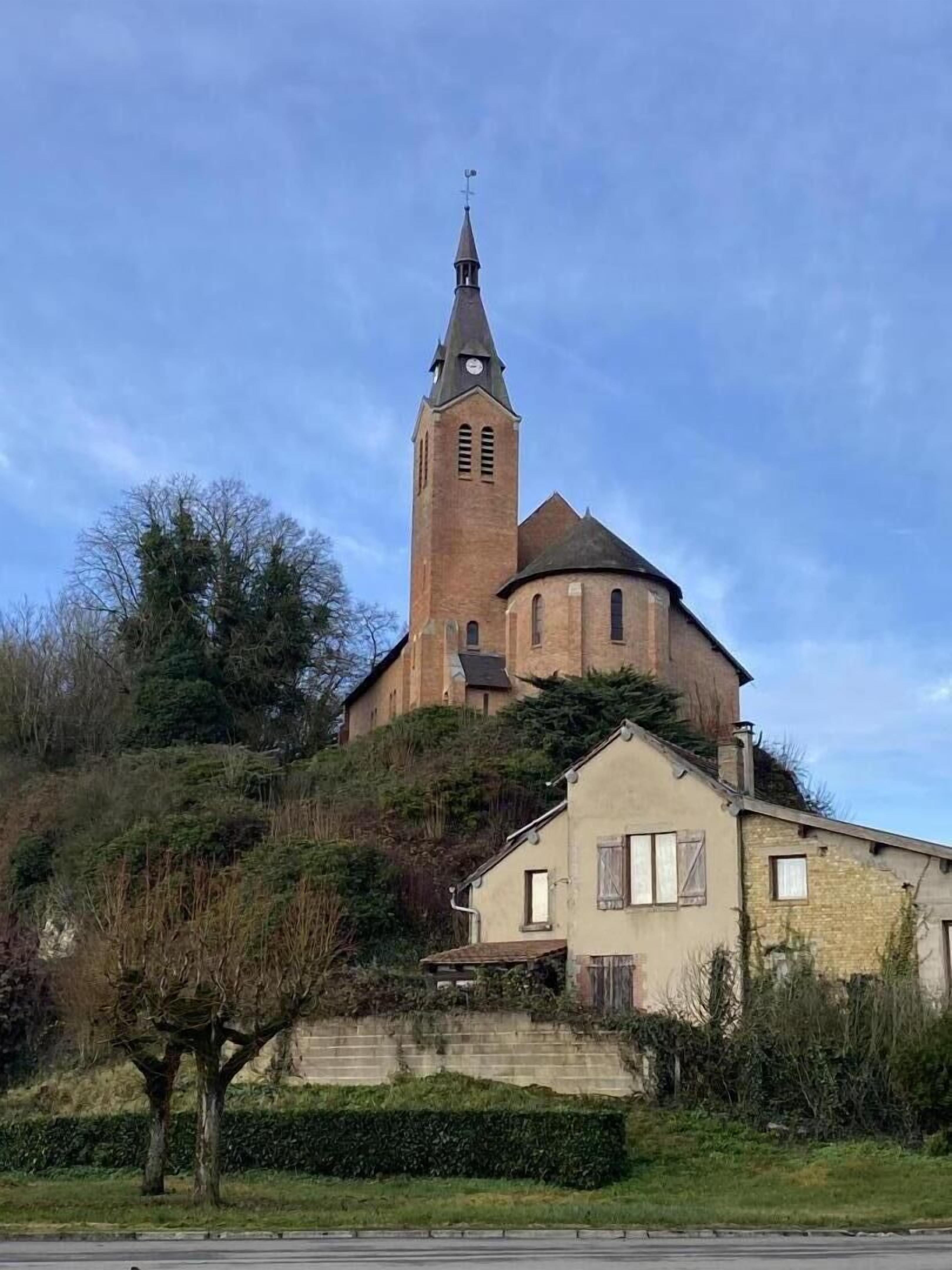 Une église dotée d’un haut clocher et d’un bâtiment plus petit situé sur une colline.