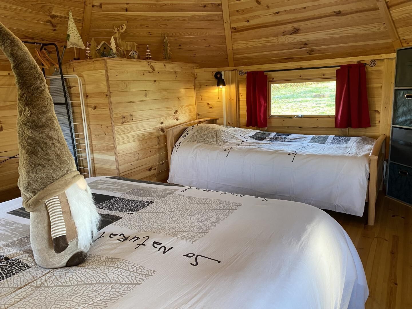 A cozy cabin with a wooden interior, a bed with a quilt, a dresser, and a window with curtains.
