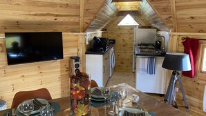 Een gezellig interieur van een blokhut met een eethoek, keuken en een aan de muur bevestigde televisie.