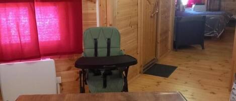 A wooden interior with a dining table and chairs, a radiator, and a window with curtains.