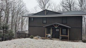 A two-story building with a dark wooden exterior, a front porch with a bench, and a small garden area with a potted plant.