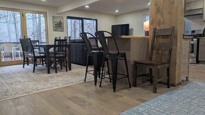 A modern kitchen with wooden cabinets, a built-in oven, and a dining area with a large window overlooking a snowy landscape.