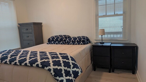 A bedroom with a bed, a dresser, a nightstand, and a lamp.