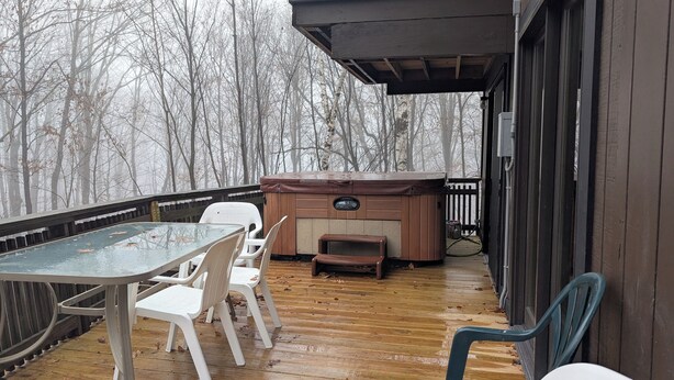 A wooden deck with a hot tub, a table, and chairs.