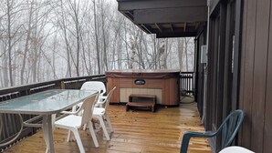 A wooden deck with a hot tub, a table, and chairs.