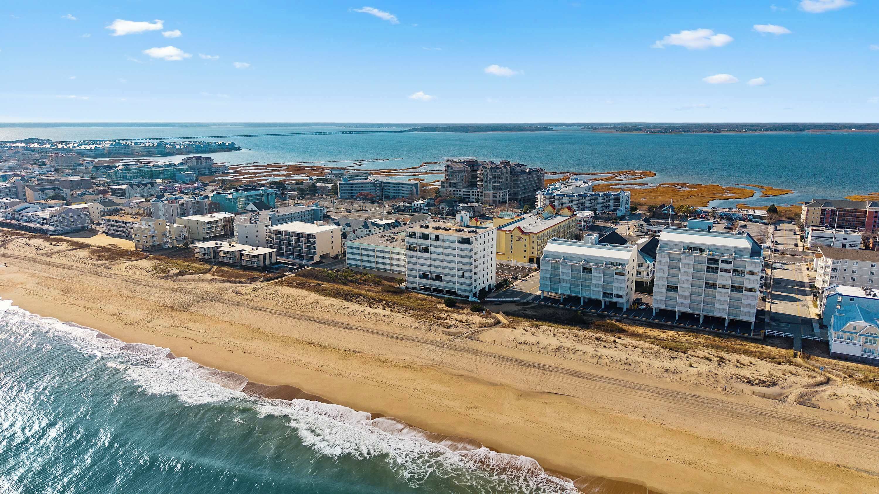 An aerial view of a coastal town with beachfront hotels, a pier, and a sandy beach.