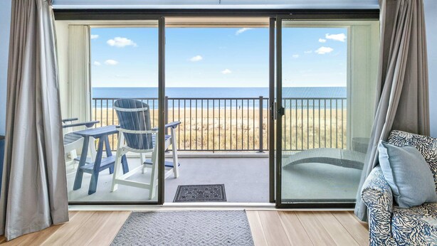 Een kamer met een grote schuifglazen deur die leidt naar een balkon met uitzicht op het strand.