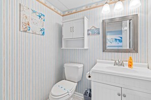 A bathroom with striped wallpaper, a toilet, a cabinet, a sink with a mirror, and a starfish decoration. - Golden Surf 203 (Ocean City)