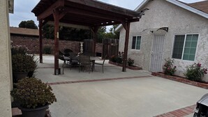 Una veranda coperta con tavolo e sedie, piante in vaso e un'auto parcheggiata nelle vicinanze.