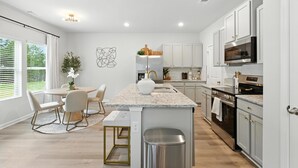 Cocina moderna con armarios blancos, encimeras de granito, electrodomésticos de acero inoxidable y una isla central con asientos.