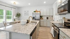Una cocina moderna con encimeras de granito, electrodomésticos de acero inoxidable y armarios blancos.