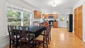 A spacious kitchen with wooden cabinets, a dining table with chairs, and a large window providing natural light. - New listing! The Terra Cotta Bungalow with Firepit! (Athens)