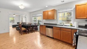 A modern kitchen with wooden cabinets, a dishwasher, and a dining area with a table and chairs. - New listing! The Terra Cotta Bungalow with Firepit! (Athens)