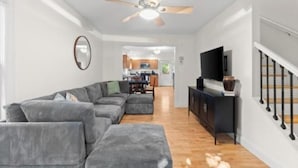 A modern living room with a sectional sofa, a ceiling fan, and a TV on a black stand. - New listing! The Terra Cotta Bungalow with Firepit! (Athens)
