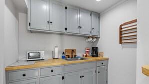 A kitchen with grey cabinets, a wooden countertop, a toaster, a sink, and a coffee maker.