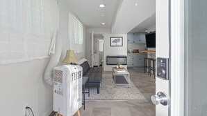 A modern living room with a sofa, a small coffee table, and a white heater. There is a kitchen area with cabinets and a television.