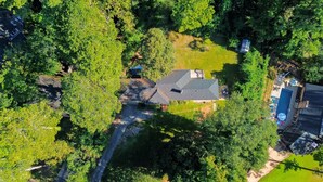 An aerial view of a residential area with a house featuring a sloped roof, a swimming pool, and a well-maintained lawn.