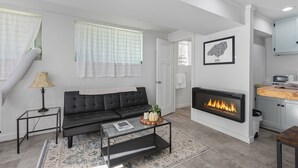 A modern living room with a black sofa, a glass coffee table, a fireplace, and a kitchen area with a microwave.