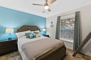 A bedroom with a bed, two bedside tables with lamps, a ceiling fan, a window with blinds, and a wall anchor decoration. - Hartwell Haus with Dock & Playground (Fair Play)