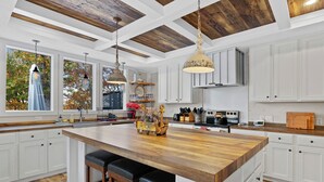 A spacious kitchen with a large island, wooden ceiling beams, white cabinetry, and pendant lighting. - Hartwell Haus with Dock & Playground (Fair Play)