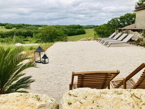 Une terrasse en gravier, agrémentée de chaises longues et d’une lanterne, qui offre une vue sur un paysage verdoyant et luxuriant.