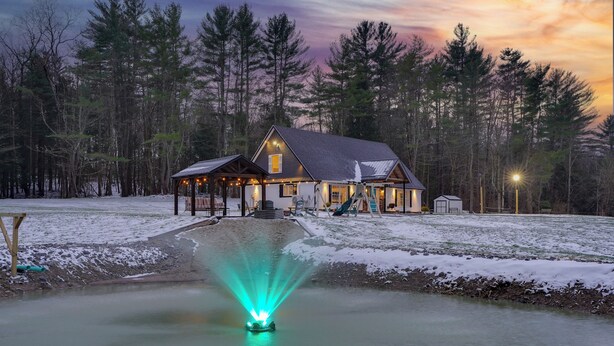 A lodge with a covered outdoor area, a pond with a fountain, and a snowy landscape.