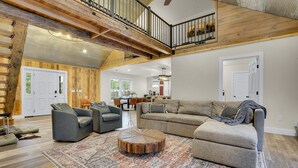 A spacious living room with a high ceiling, exposed wooden beams, a round coffee table, and a large sofa.