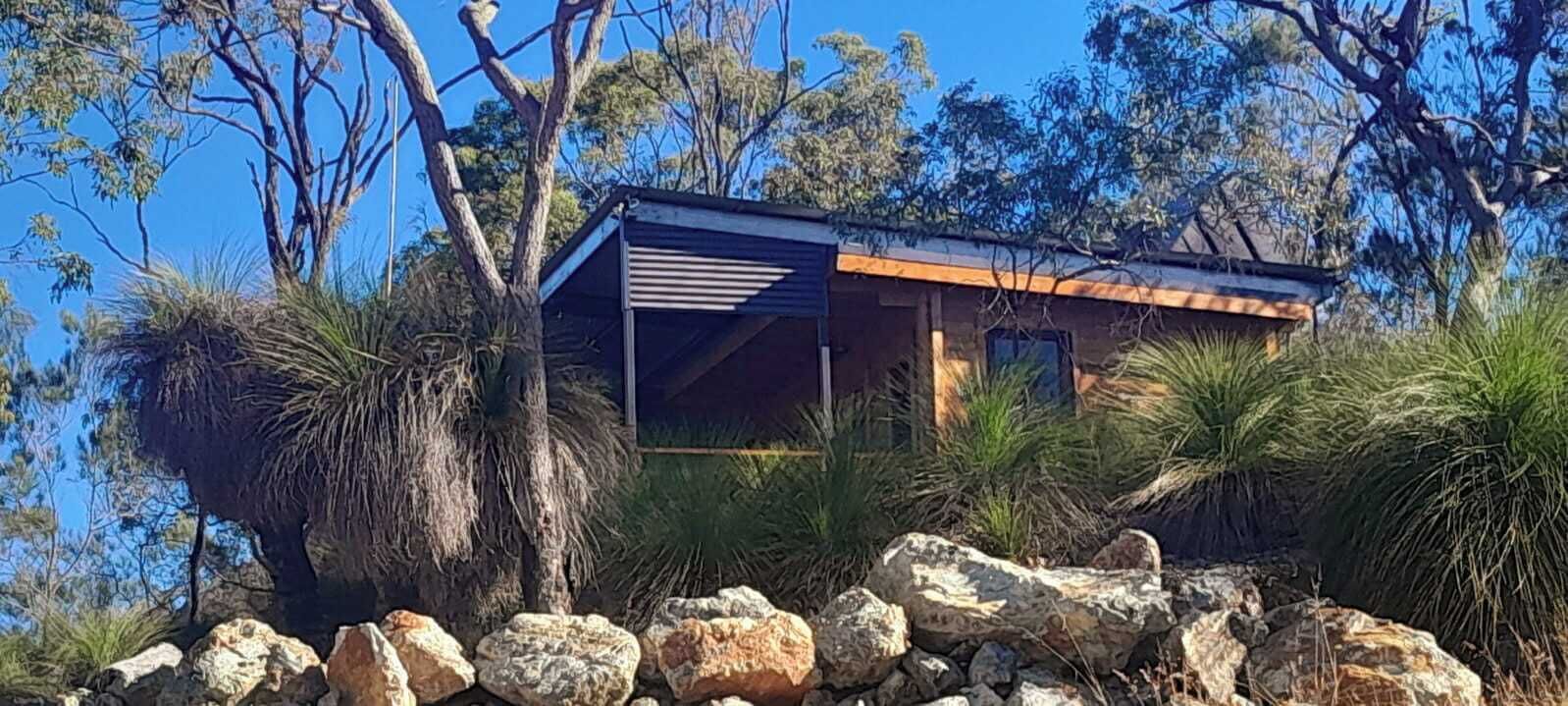 A modern building with a flat roof, surrounded by natural vegetation and rocks.