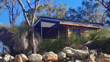 A modern building with a flat roof, surrounded by natural vegetation and rocks.