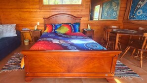 Een slaapkamer in een houten hutje, met een bed, een tafeltje, stoelen en een raam.