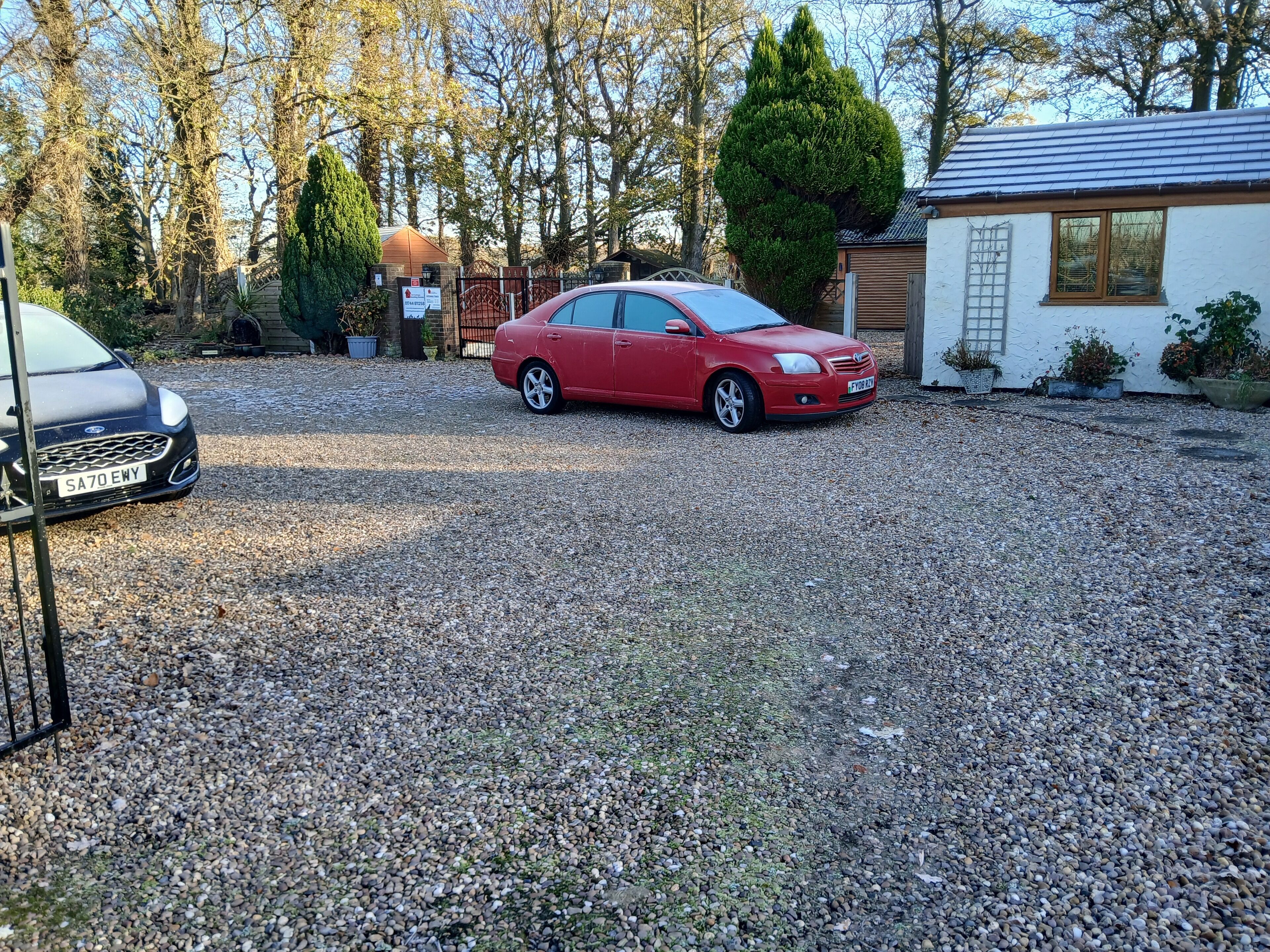 A gravel driveway with a red car parked in the middle.