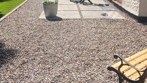 A patio area with a gravel surface, a wooden bench, a potted plant, and a grill in the background. - Park Cottage Bed & Breakfast near Burtonwood (Saint Helens)
