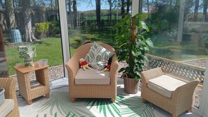 A wicker chair with a cushion and a small table with a plant, both on a balcony with a view of a garden. - Park Cottage Bed & Breakfast near Burtonwood (Saint Helens)
