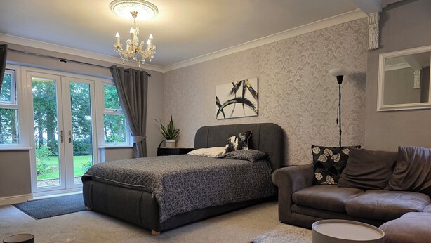 A modern bedroom with a bed, a sofa, a small table with cups, and a chandelier. - Park Cottage Bed & Breakfast near Burtonwood (Saint Helens)
