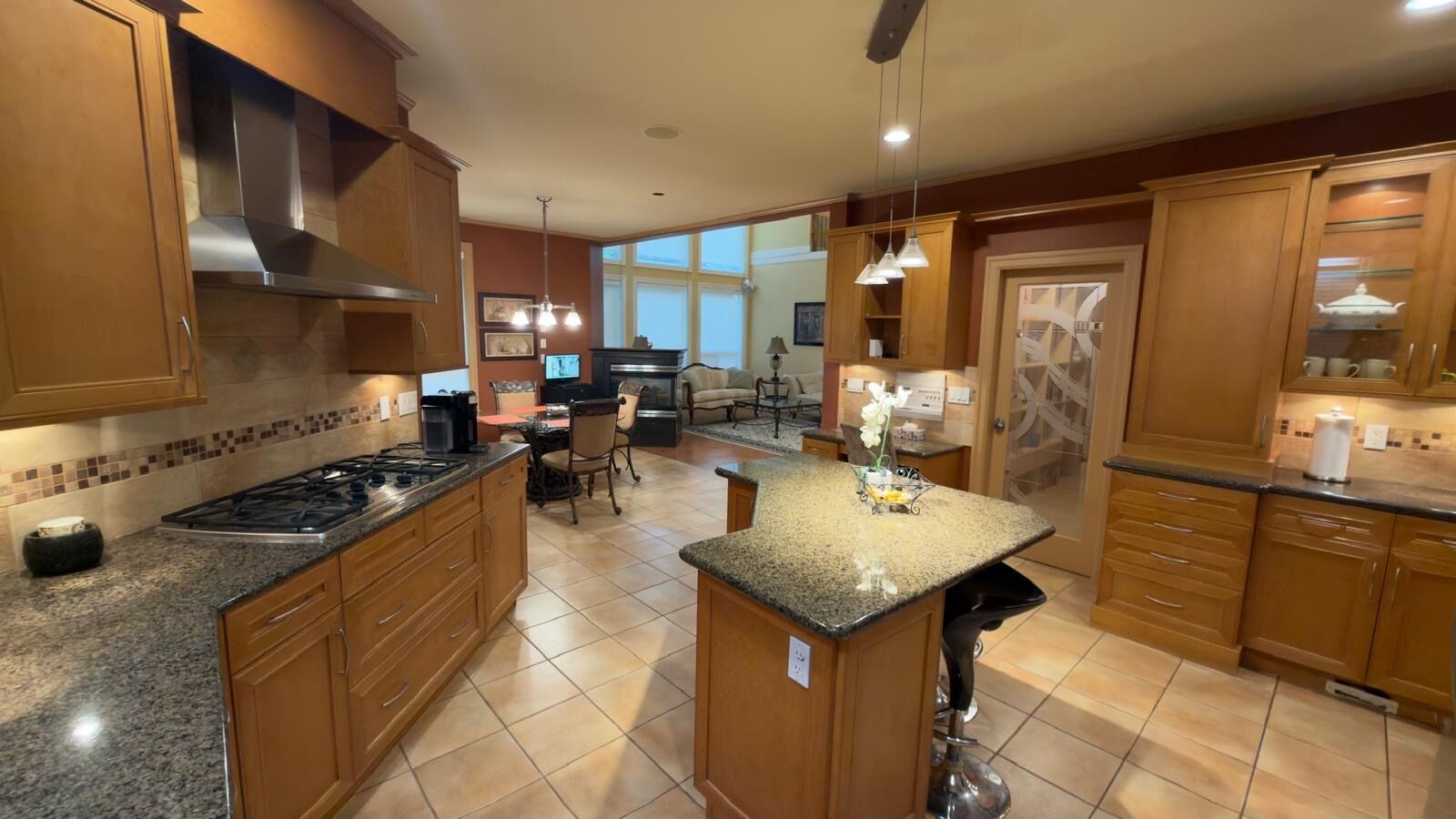 A kitchen with granite countertops, wooden cabinets, a central island, and a dining area with chairs.