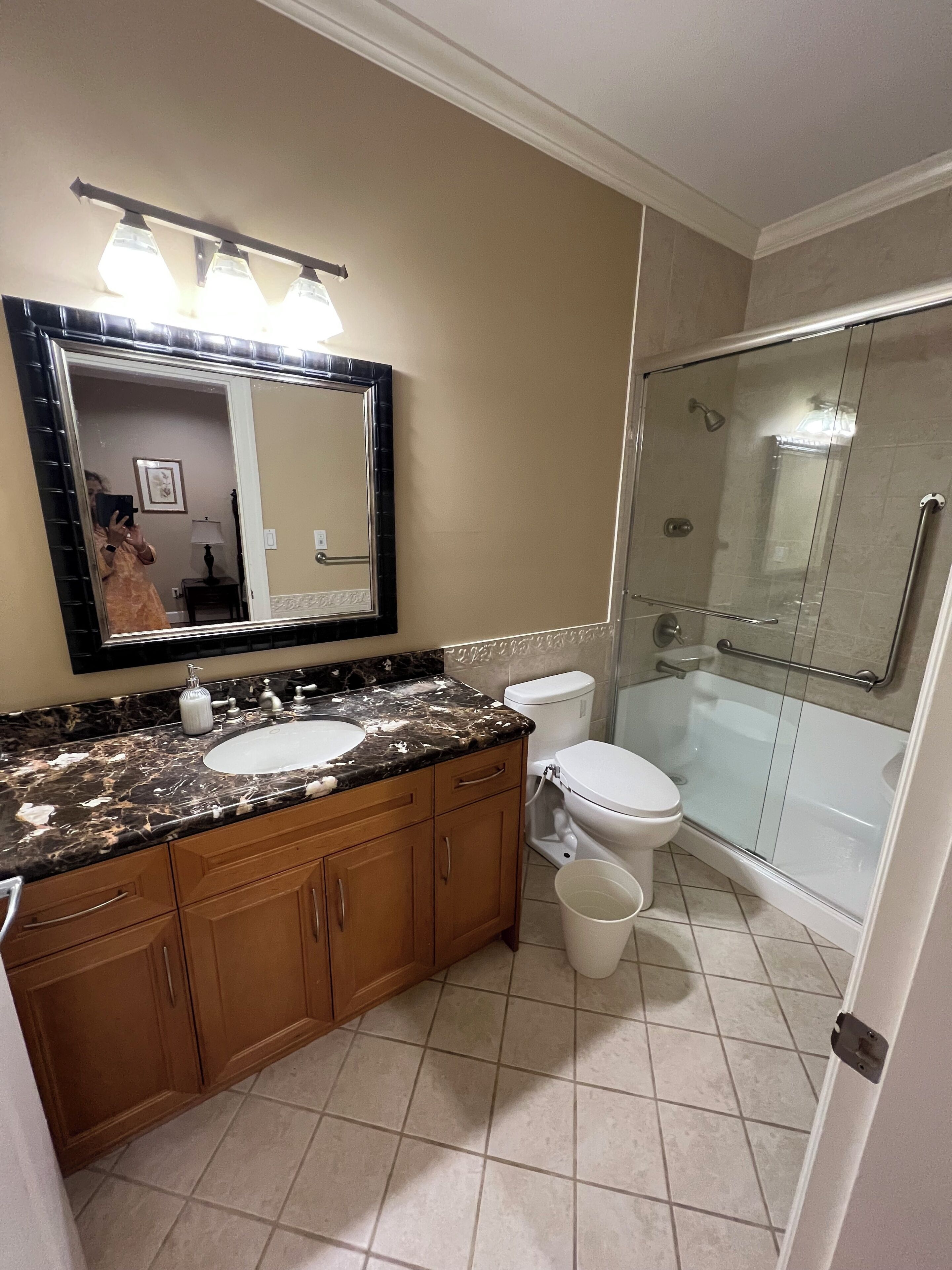 A bathroom with a double sink vanity, a toilet, a glass-enclosed shower, and a large mirror with lights above.